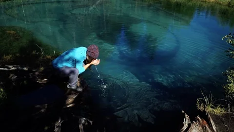 Young tourist in a hat with backpack is drinking and washing from the cold blue Stock Footage 96441973