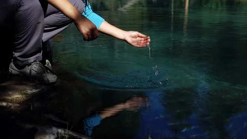 Young tourist in a hat with backpack is drinking and washing from the cold blue Stock Footage 96442530