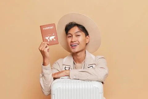 Young tourist man in hat with white suitcase showing his passport with wide Stock Photos