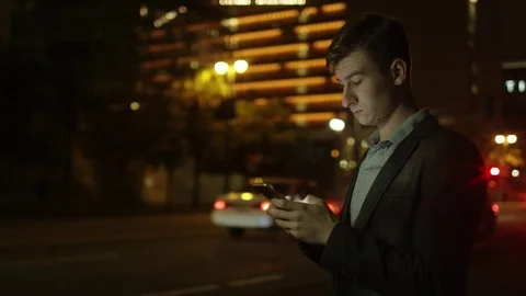 Young tourist is texting while standing on a street at night Stock Footage 77577828