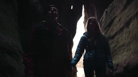 Young tourists studying the dark cave, holding their hands, and moving towards Stock Footage 73885477