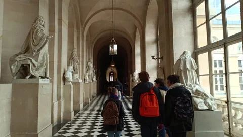 Young tourists walking down a long historic corridor with statues in Versailles Stock Footage 341928073