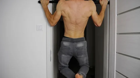 Young trained and athletic man is doing pull ups in his door frame at home Stock Footage 122040050