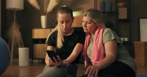 The young trainer and her protegee sit on a yoga mat watching on their phones Stockbeeldmateriaal 218877692