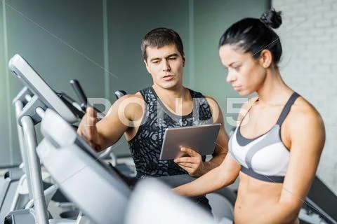 Young trainer explaining how to regulate speed of treadmill to active girl Stock Photos