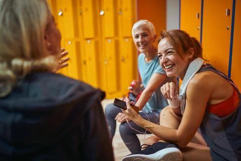 Young trainer talking with two senior woman in dressing room, after trainin.. Stock Photos