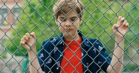 Young transgender boy looking through a chain link fence Stock Footage 108789456