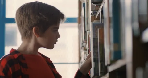 Young transgender boy selecting a book in a library at school Stock Footage 108788726