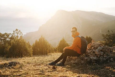 Young traveler with backpack resting while walking at sunset. Stock Photos