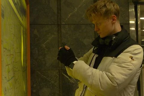 Young traveler examines subway map with concentrated focus in winter gear 스톡 사진