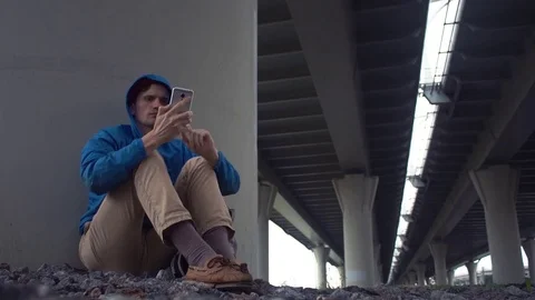 Young traveler using smartphone sitting on the ground under road bridge Stock Footage 80285929