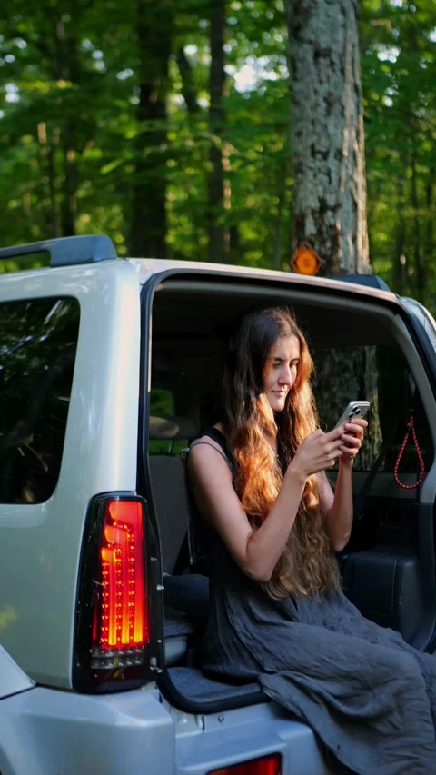 Young traveler using a smartphone from an SUV in a woodland setting. 库存影片 340290980