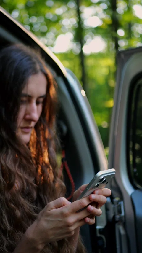 Young traveler using a smartphone from an SUV in a woodland setting. Видео 340291008