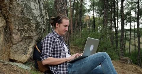 Young traveling man with backpack using laptop to work remotely in forest. Stock Footage 151859692