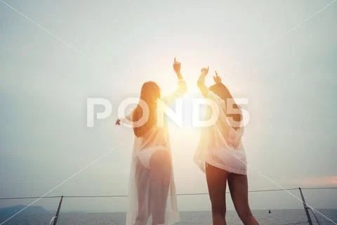 Young two girl friends raising hands up wearing summer bikini against sun light Stock Photos