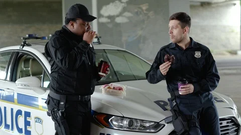 Young two policemen speak drinking coffee and eating donut with appetite talk Stock Footage 112956557