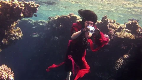 Young underwater model free diver in red dress photographs on camera in Red Sea. Stock Footage