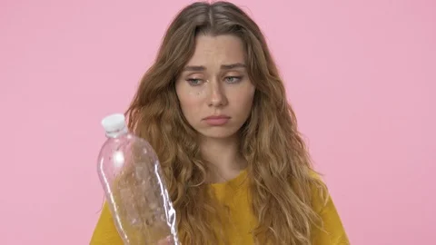 A young unhappy woman in basic t-shirt is holding plastic bottle and crying 스톡 동영상 124956421