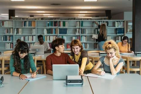 Young university students using laptop and studying with books in library Stock Photos