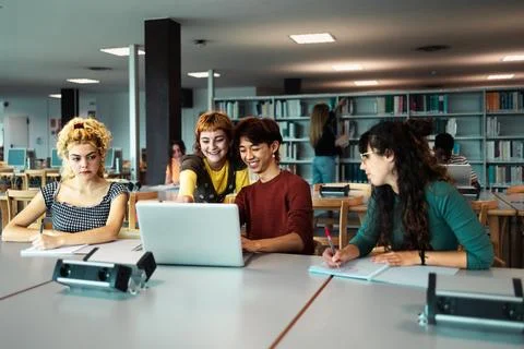 Young university students using laptop and studying with books in library Stock Photos