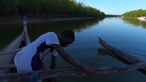 A young unknown Malagasy man sits in typical canoe near local fishing village Stock Footage 310062884