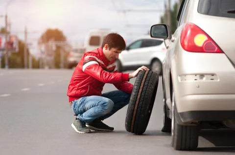 Young upset man changing tyre wheel on cityroad Stock Photos
