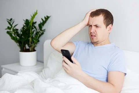 Young upset man using smartphone in bed Фото