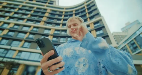 A young urban man is using his smartphone amidst the bustling modern cityscape Stock Footage 303431704