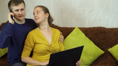 Young using laptop while sitting on sofa at home. Guy talking on the phone Stock Footage 99402561