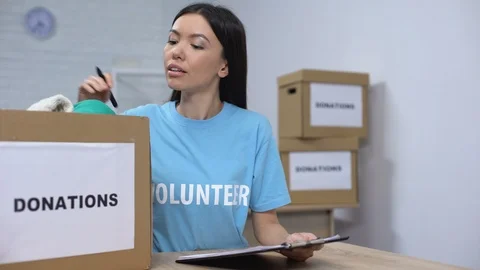 Young volunteer checking clothes donation box and making notes, humanitarian aid Stock Footage 113389758