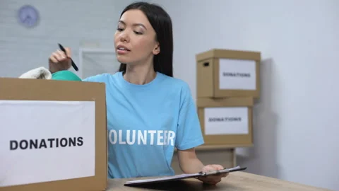 Young volunteer checking clothes donation box and making notes, humanitarian aid Stock Footage 113399155