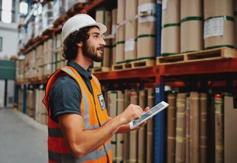 Young warehouse worker in hardhat and safety jacket using digital tablet while Stock Photos