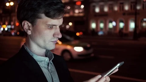 Young wearing casual man using smartphone on a busy urban street at night Stock Footage 80009706