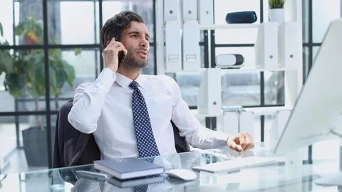 Young web developer talking on phone while working with laptop in office Stock Photos