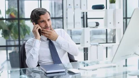 Young web developer talking on phone while working with laptop in office Stock Photos