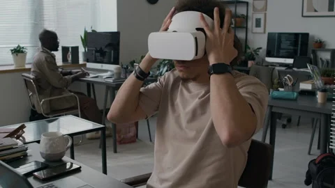 Young Web Engineer Putting on VR Headset while Working on Laptop in Office Stock Footage 299232338