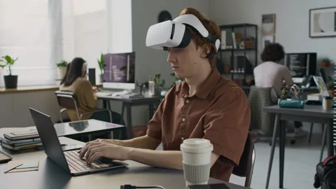 Young Web Engineer Using VR Glasses to Do Programming on Laptop at Work Desk Video stock 299247974