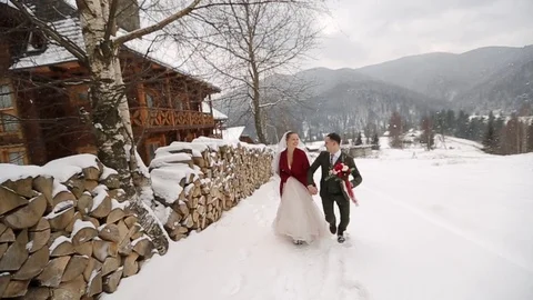 Young wedding couple running, having fun holding hands at ski resort village Stock Footage 100271417