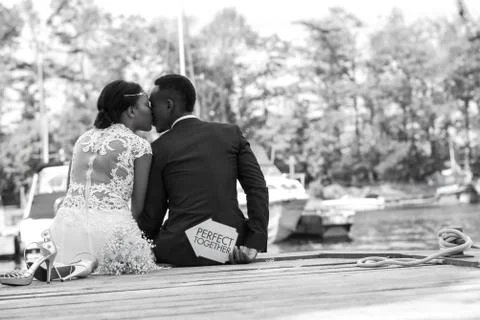Young wedding couple sitting at a wooden dock and kissing Stock Photos