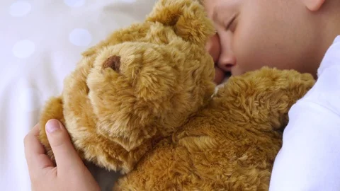 Young white kid sleeping laying in his bed with cute brown teddy bear toy 動画素材 94225366