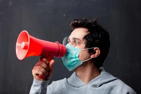 Young white man in glasses and protective mask with loudspeaker Stock Photos