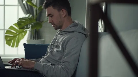A young white man sits on the couch with a laptop and works 库存影片 127413847