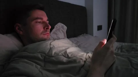 Young white man using smartphone while lying in bed at night Stock Footage 284042558