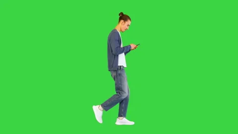 Young white man walks typing something on his smartphone on a Green Screen Vídeos de archivo 157076096