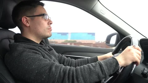A young white man without a beard and wearing glasses driving a car on the Stock Footage 155779165