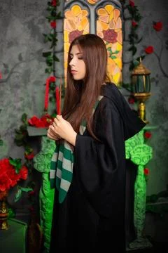 A young witch in a black cloak with a magic wand in her hands conjures a spell Stock Photos