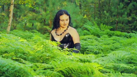 A young witch in black clothes is standing in a forest in a thicket of fern Stock Footage 94232338