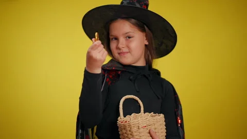 A young witch is joyously holding a vibrant basket filled with delightful Stock Footage 315412530