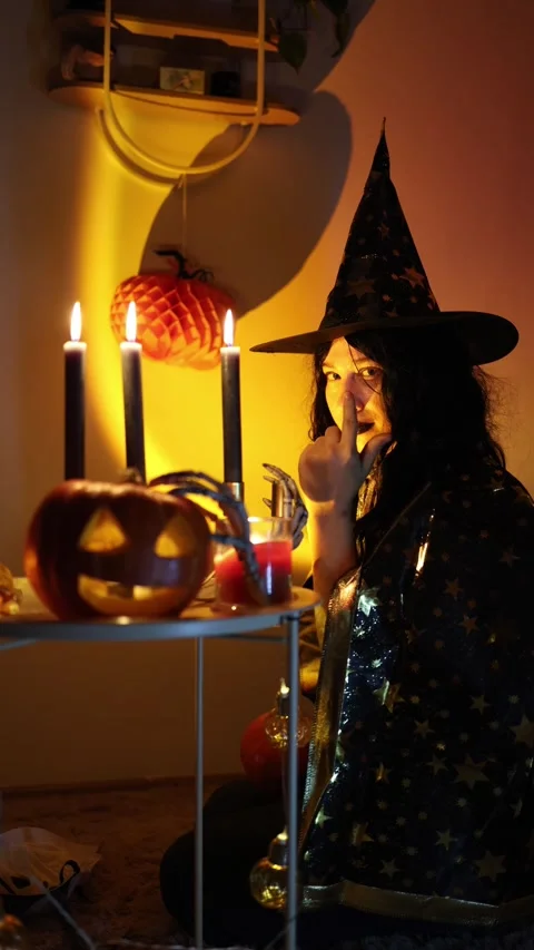 Young witch makes mysterious gesture toward camera at Halloween party Stock Footage 345494165