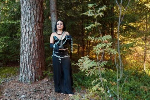 A young witch in the woods chained to a tree. Halloween. Fotos Stock